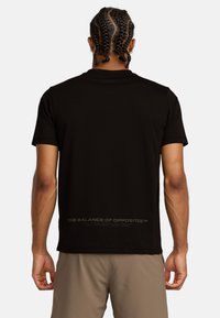 T-shirt nera a maniche corte con scollatura rotonda; presenta una stampa testuale lungo la parte bassa della schiena. Tessuto morbido con un design aderente.