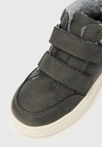 Γκρι συνθετικό ψηλό αθλητικό παπούτσι με τρεις λουριά Velcro και μαλακή, γούνινη επένδυση. Διαθέτει λευκή ελαστική σόλα και υφασμένη επιφάνεια.