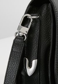 Borsa a tracolla in pelle nera con superficie testurizzata, con chiusura metallica argentata e un distintivo dettaglio metallico a forma di V.