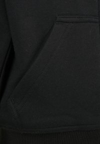 Primer plano de un bolsillo de tela negra con costuras visibles en una prenda de ropa, probablemente una sudadera o una sudadera con capucha.
