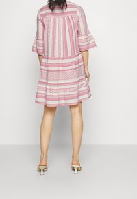 Robe fluide en forme trapèze en tissu léger, ornée de motifs géométriques rouges et de manches à volants. Le dos présente un plissage pour plus de texture.