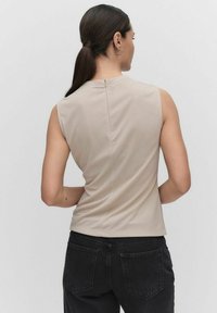 Beige ærmeløs top med en glat tekstur, lynlås lukning bagpå og en tætsiddende pasform. Kombinationen med mørke jeans med baglommer.