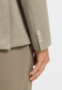 Helle beige strukturierte Blazer mit Reverskragen, ausgestattet mit fünf hellen Knöpfen am Ärmel, kombiniert mit einer passenden maßgeschneiderten Hose.