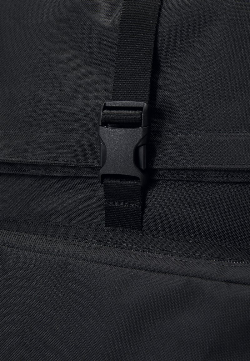 Sort nylon rygsæk med en struktureret overflade, der har en plastspænde lukning og justerbar rem. Minimalistisk design uden synlige mønstre.