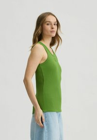 Green ribbed tank top with a scoop neck and wide straps, paired with a light blue denim skirt, shown from the side.