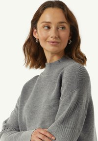 Grau gerippter Strickpullover mit hohem Kragen und überschnittenen Schultern. Weicher Textur und lockere Passform. Dezente Nahtdetails an den Schultern.