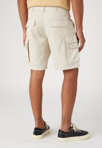 Pantaloni cargo beige con due tasche laterali e due tasche posteriori, realizzati in tessuto leggero, con una vestibilità rilassata e dettagli cuciti.