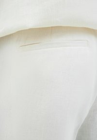 Białe lniane spodnie o fakturowanym wykończeniu, z kieszenią na dziurkę po prawej stronie i prostym krojem.