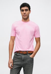 Tricou cu mânecă scurtă și gât rotund din bumbac roz deschis, asortat cu blugi gri închis și curea maro. Design simplu, cu culoare uniformă.