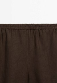 Pantalon en lin de couleur marron foncé avec taille élastique et couture centrale, présenté à plat sur un fond blanc.