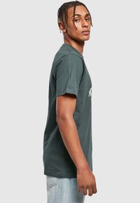 Grå bomulds T-shirt med rund hals, korte ærmer og et subtilt grafisk design på fronten, parret med lyse denim jeans.
