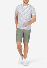 White short-sleeve shirt with a floral pattern, paired with olive green cargo shorts. Model wears white sneakers, displaying a relaxed fit.