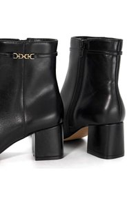 Black leather ankle boots with a block heel, side zipper, and a decorative gold chain accent on the ankle. Smooth texture and fitted design.