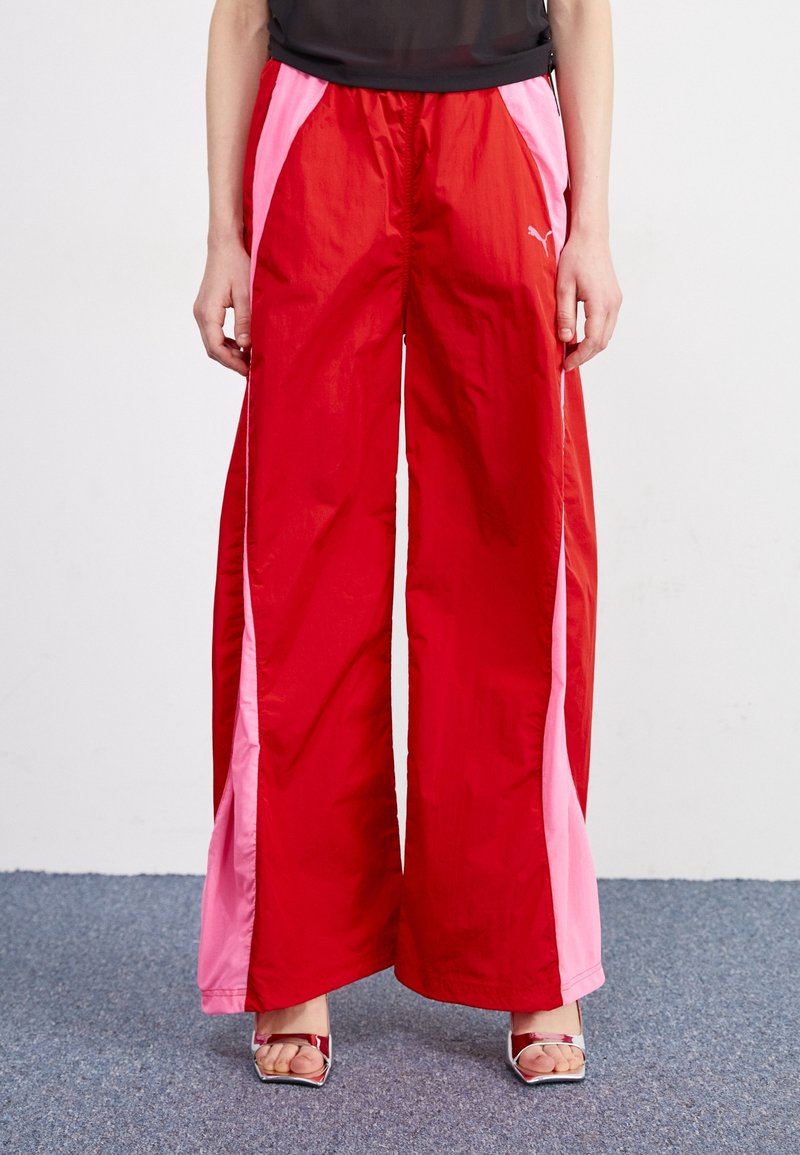 Pantalons de sport rouges avec des panneaux latéraux roses, fabriqués en matériau léger. Dotés d'une taille élastique et d'une coupe large et décontractée.