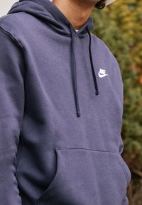 Navy blue hoodie made of cotton blend, featuring a front pocket, drawstring hood, and a white Nike logo on the chest. Soft texture.