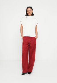 Biały top z krótkim rękawem i wysokim dekoltem, zestawiony z szerokimi czerwonymi spodniami i czarnymi, spiczastymi szpilkami. Gładka tkanina o prostym wzorze.