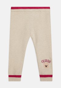 Leggings beige con una consistenza morbida, vita e polsini a coste rossi, con una grafica di un orso e il testo "GUESS" ricamato in bordeaux.