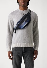 Juodas ir mėlynas nailono crossbody krepšys su užtrauktuku, kuriame ant priekinės dalies ir dirželio yra grafinių atvaizdų ir balto teksto "KARL LAGERFELD JEANS".