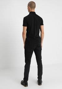 Polo noir à col classique, design ajusté et manches courtes, associé à un jean noir et des bottes en cuir. Détails visibles au dos.