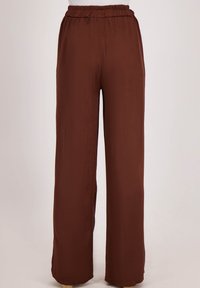 Koffiekleurige, wijde broek van een lichtgewicht, glad materiaal. Voorzien van een elastische tailleband en geen zakken voor een minimalistisch ontwerp.