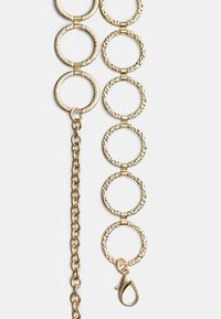 Goldene Kettenaccessoire mit strukturierten runden Gliedern und einem Karabinerhaken. Das Design umfasst glatte und gemusterte Elemente.