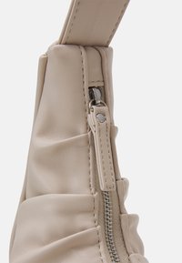 Beżowa skórzana torba o marszczonej fakturze, z widocznym zapięciem na zamek i kontrastowym przeszyciem. Gładka powierzchnia z metalowymi detalami.
