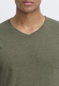 Olivgrünes V-Ausschnitt-T-Shirt aus weichem, strukturiertem Stoff, das einen lockeren Schnitt und minimale Nähte rund um den Ausschnitt aufweist.
