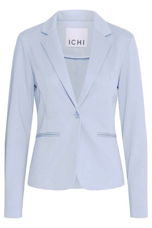 Personne portant un blazer bleu clair à un bouton et un jean en denim bleu clair, debout devant un fond uni.