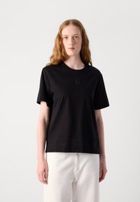 Svart bomulls t-skjorte med rund hals og korte ermer, med en subtil brodert design på brystet. Glatt tekstur, avslappet passform.