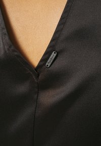 Crna satenska tkanina s dizajnom u obliku V-izreza, s malom crnom etiketom s natpisom "Pepe Jeans" blizu izreza. Glatka tekstura i minimalno šivanje.