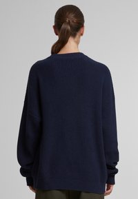 Maglione blu navy lavorato a maglia con una vestibilità ampia, spalle scese, colletto e polsini a costine, che mette in mostra un tessuto testurizzato e una silhouette rilassata.