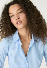 Camicia a maniche lunghe blu con righe, dotata di colletto classico, con un design aderente e una trama liscia. La camicia presenta righe verticali di un blu chiaro e bianco.