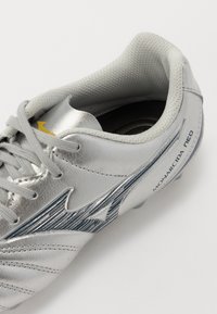 Scarpa da calcio argento con tomaia in pelle, design testurizzato, accenti blu e lacci grigi. Presenta il logo e il nome del modello sul lato.