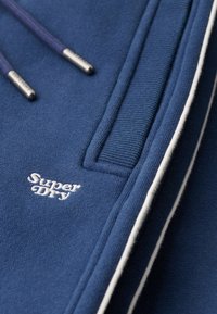 Blauwe sweatshirt met witte accenten, gebreide textuur en logo geborduurd in het wit. Voorzien van aantrekkoorden met metalen uiteinden.