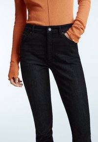 Svarta jeans med slim fit och femfickorsdesign. Tyget är mjukt med en lätt stretch. Matchas med en figurnära långärmad topp i orange.