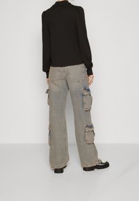 Schwarzes Langarmshirt mit Kragen, kombiniert mit hellgrauen Cargo-Hosen mit seitlichen Taschen und sichtbaren Nahtdetails. Bulky schwarze Stiefel.