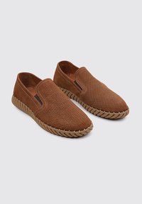 Chaussettes en daim marron à enfiler avec un design perforé, présentant une semelle en caoutchouc texturé tan et des accents cousus le long des bords.