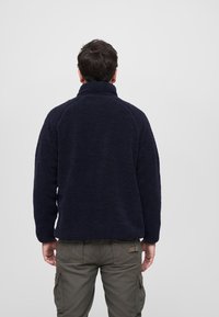 Pullover in pile blu navy con colletto alto, tessuto testurizzato e maniche raglan; abbinato a pantaloni cargo verde oliva.