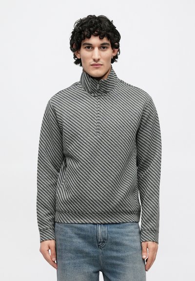 Sivý pulóver so vzorom a vysokým golierom, zdobený textúrovaným diagonálnym pruhovaním. Materiál je mäkký a pružný.