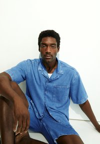 Bordeaux denim overhemd met korte mouwen en een borstzak, gecombineerd met bijpassende shorts. Zachte textuur en knoopsluitingen.