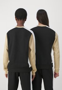 Felpe girocollo in nero, beige e bianco con un design a blocchi di colore. Il tessuto sembra morbido con una vestibilità rilassata e polsini a costine.