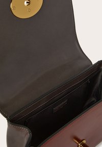 Borsa a tracolla in pelle marrone con una chiusura circolare dorata e una superficie liscia. L'interno presenta una fodera nera e una tasca laterale per un migliore organizzazione.