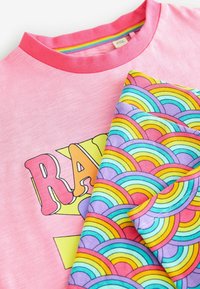 Camiseta rosa con la palabra "RAINBOW" en letras grandes, combinada con una tela multicolor de patrón arcoíris con líneas curvas.