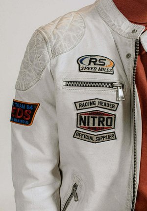 Veste en cuir gris clair avec un détail matelassé aux épaules, plusieurs patchs brodés, une poche zippée et une finition texturée.