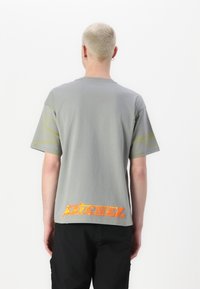 Grå bomulls t-skjorte med korte ermer, med abstrakte gule mønstre på ermene og en oransje "Diesel" logo på baksiden. Enkel design.