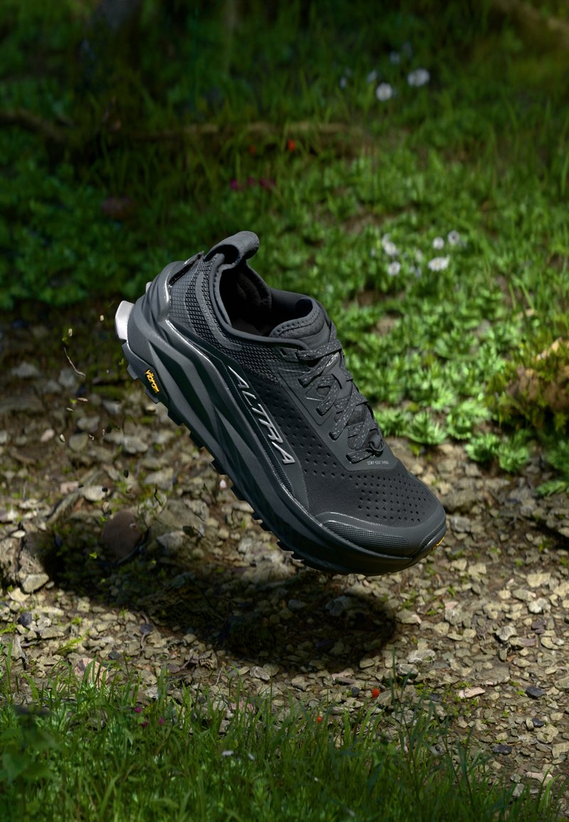 Zwarte trailrunning schoen met een gestructureerde bovenkant, opvallende dempingzool en Vibram-buitenzool, gepresenteerd in een natuurlijke buitenomgeving.