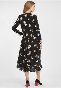 Zwarte bloemenjurk met lange mouwen en een gelaagde rok. Heeft roze en witte bloemenpatronen, gemaakt van lichte stof. Gecombineerd met zwarte hakken.