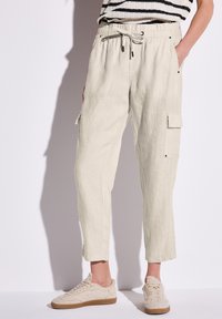 Helle beige Leinen-Cargohosen mit elastischem Bund, Kordelzug, Seitentaschen und schmal zulaufendem Bein. Kombiniert mit neutralen Sneakern.