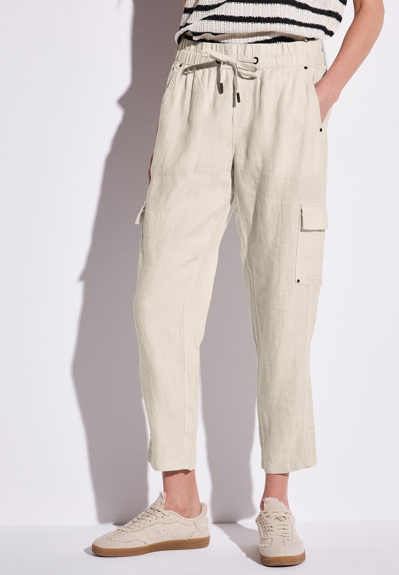 Helle beige Leinen-Cargohosen mit elastischem Bund, Kordelzug, Seitentaschen und schmal zulaufendem Bein. Kombiniert mit neutralen Sneakern.