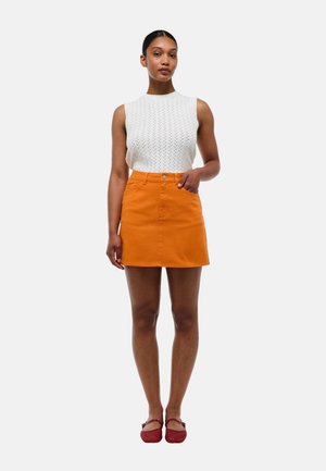 Haut sans manches en tricot blanc associé à une jupe courte évasée orange. La jupe possède un bouton à l'avant, une texture lisse et des poches latérales.